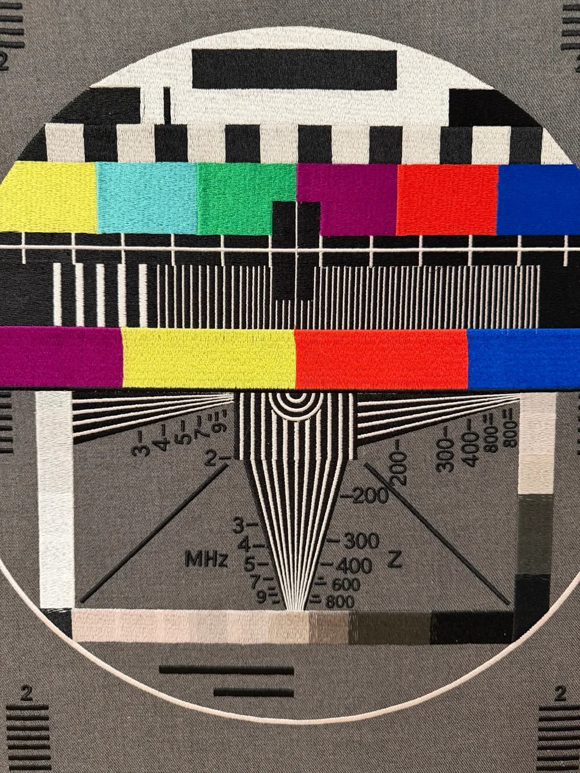 A Signal Held Still (detail) — close-up of coloured test bars, fine measuring lines and stitched calibration symbols