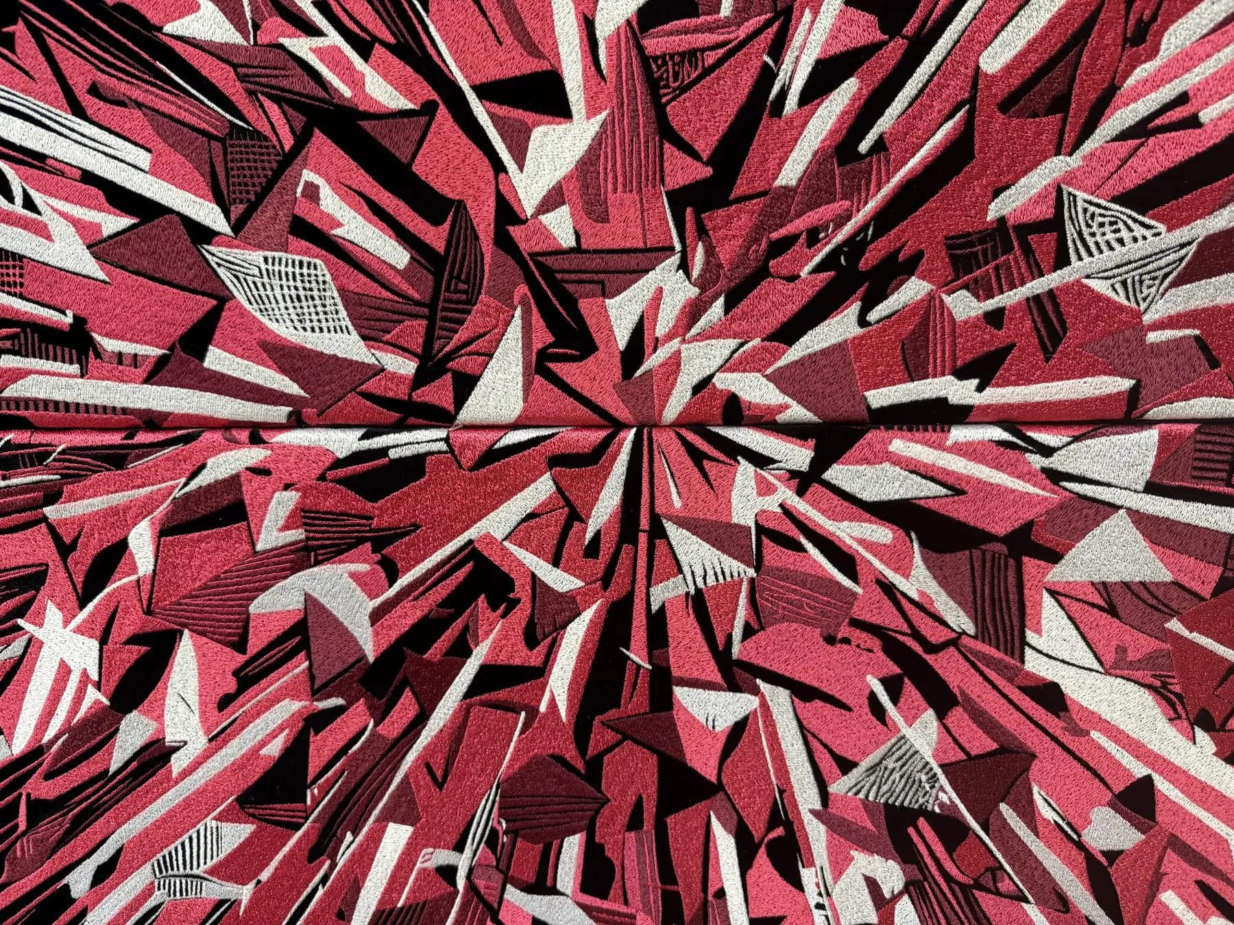 Superbloom (detail) — close-up of angular red and pink embroidered shapes converging around a central point